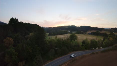 Single-Van-travels-down-empty-highway-in-farmland-during-sunset