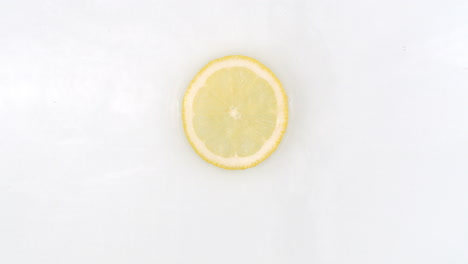 On-a-white-background-a-splash-of-water-falls-on-a-slice-of-lemon-in-slow-motion.