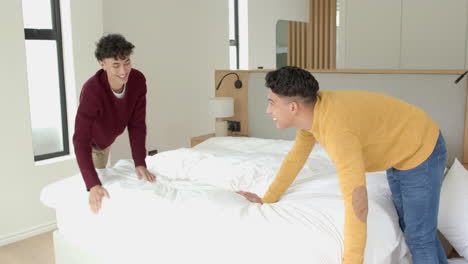 making bed , multiracial gay couple smiling and enjoying time at home