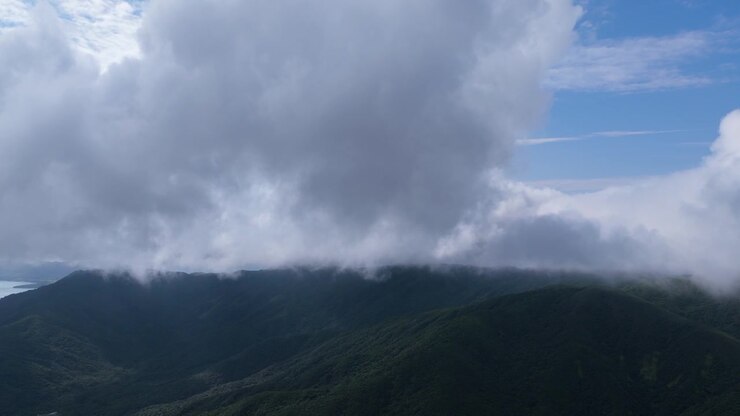 Horizontal cameo slowly tilting down toward the forested Mount Omoto ridge covered by mist and clouds in Ishigaki, Okinawa, Japan