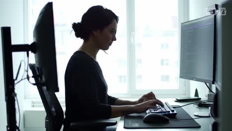 a woman sits at her desk in a well-lit home office, intently typing on her keyboard. the workspace features modern tech, emphasizing a productive atmosphere in the late afternoon.