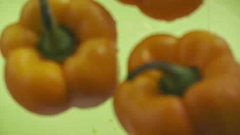 slow motion of yellow peppers falling into water surface on green background