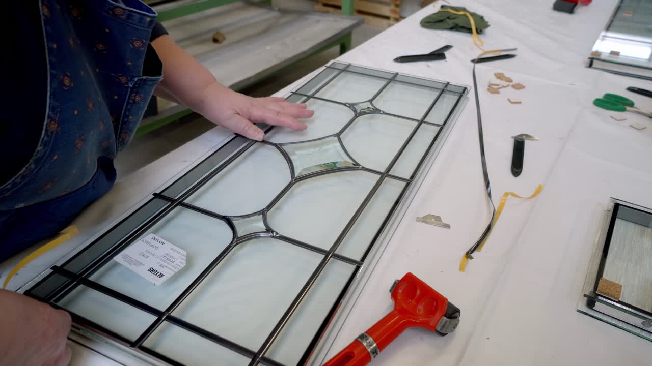 Close-up of artisan assembling stained glass panel using lead came and glass pieces on worktable