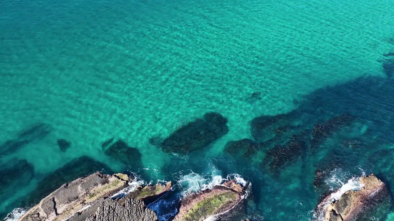 Ripresa aerea con drone dall'alto di acqua turchese cristallina e onde che si infrangono sugli scogli in Australia.
