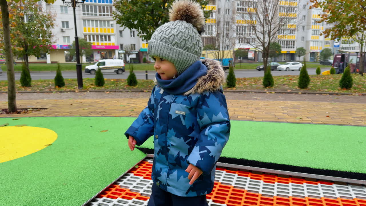 Little cute kid in warm autumn clothes jumping on trampoline. Baby boy falls, stands up and continues have fun.
