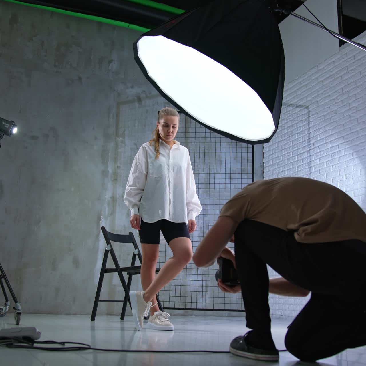 Camera man taking picture of a model in studio. Photographer squatted to take a picture of a female standing her back to him