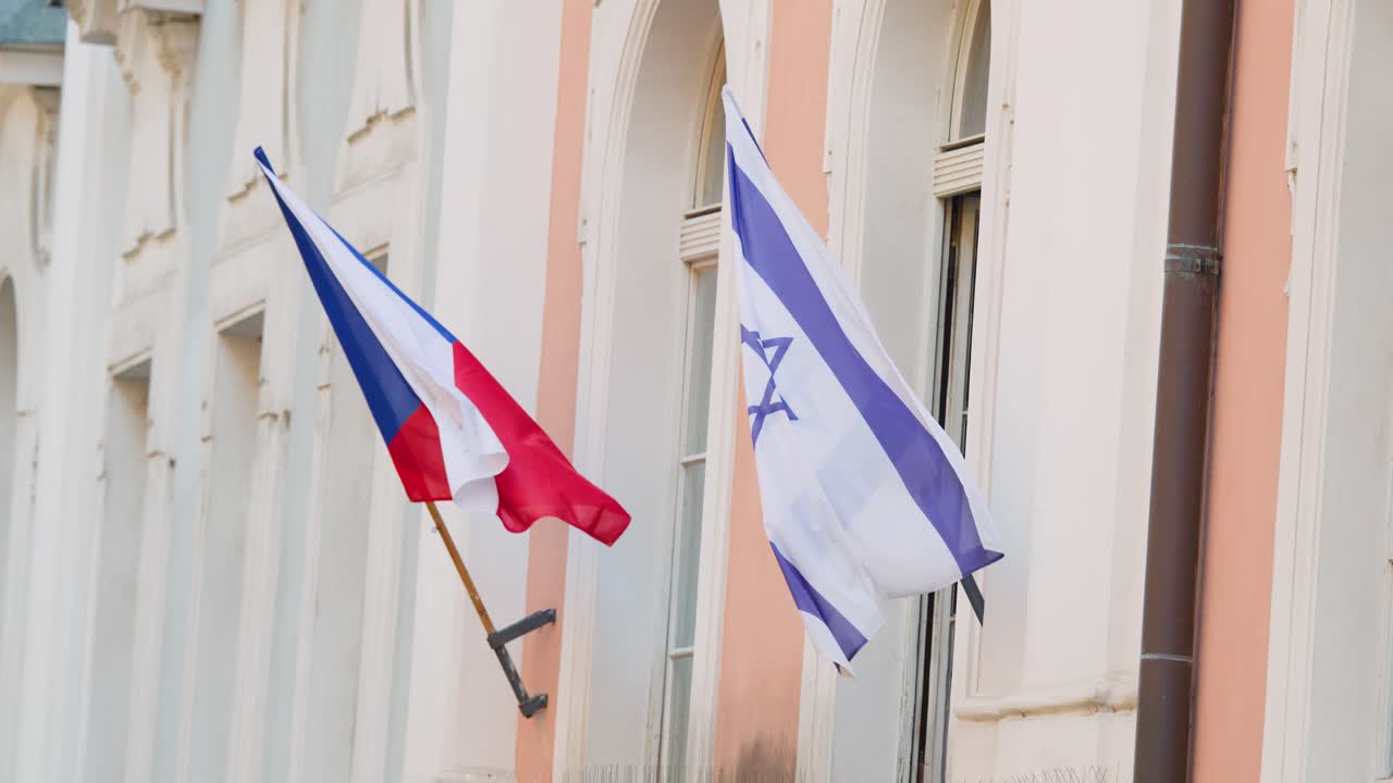 Czech and Israeli flags wave on building facade, daylight, steady camera, soft natural lighting