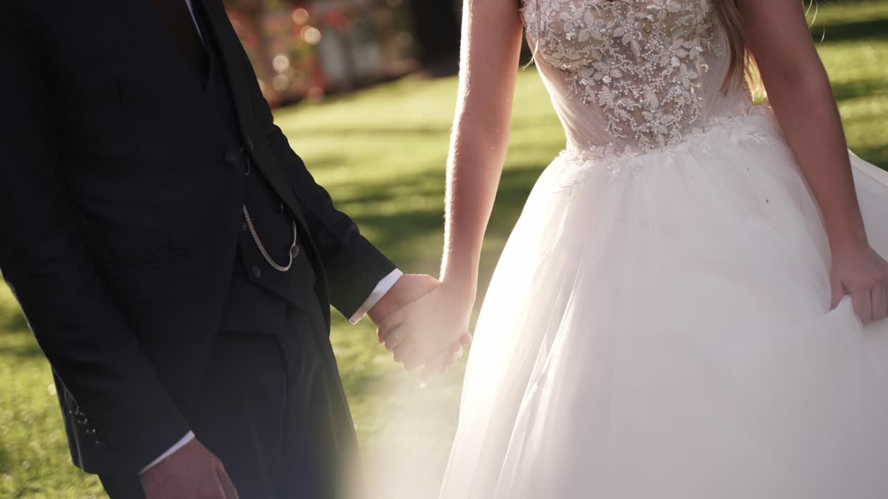 Primo piano delle mani della sposa e dello sposo unite alla luce del sole all'aperto
