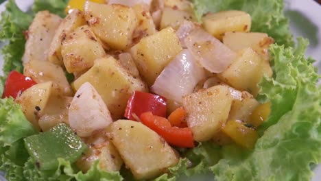 a delicious potato salad with onions, red sliced peppers and lettuce on a rotating plate with close up