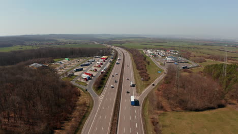 Reenvía-El-Coche-De-Seguimiento-Girando-Hacia-La-Gasolinera-Desde-La-Autopista-De-Varios-Carriles.-Paisaje-Plano-Alrededor.-Concepto-De-Tráfico-Y-Transporte.