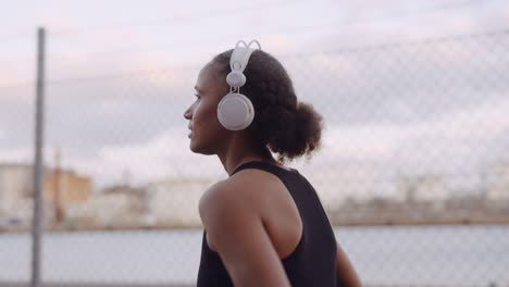 young woman in sportswear and headphones jogging along harbour