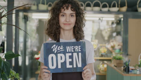 woman shopkeeper holding open sign in flower shop