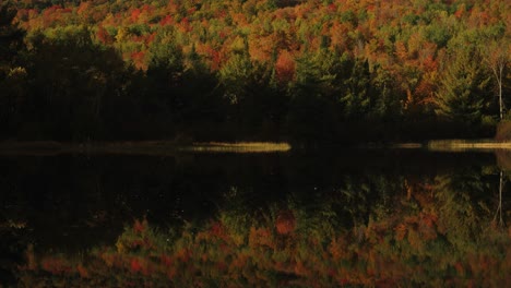 golden hour light illuminates sky and autumn foliage on mountain reflection in lake