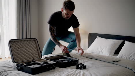 man packing camera gear into a suitcase on a bed