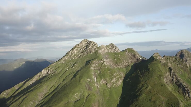 Terreno naturale di scogliere e cime montuose alla luce del sole, circondato da un cielo blu nuvoloso, paesaggio naturale