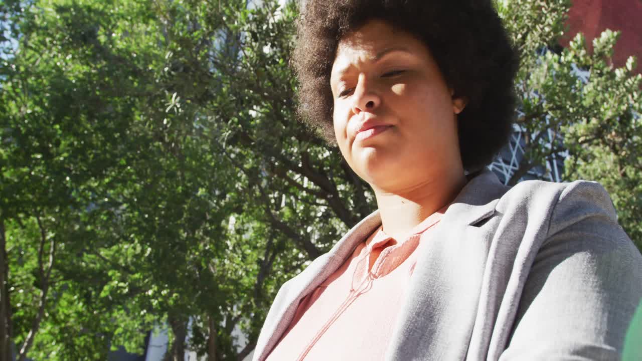 mujer biracial de talla plus chequeando el reloj inteligente y caminando por la ciudad