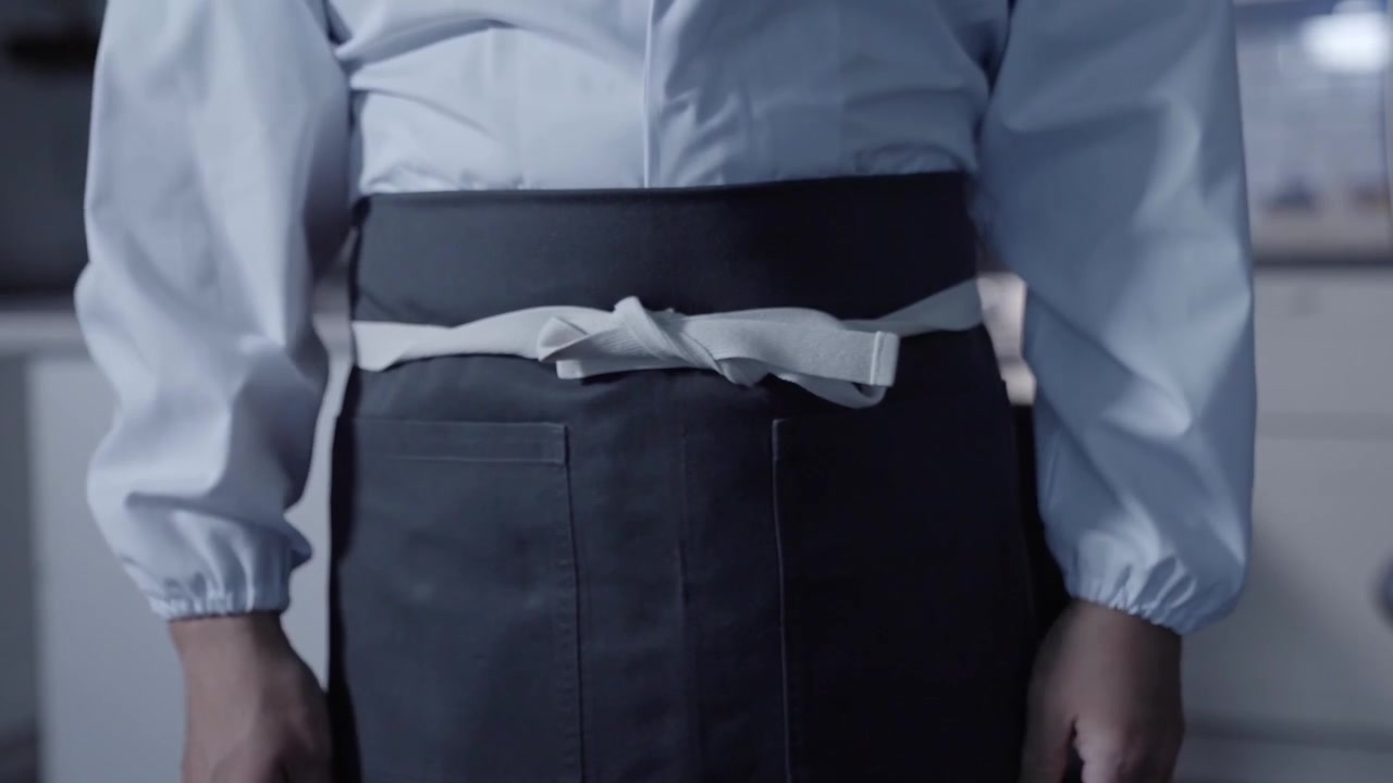 Una ripresa statica in primo piano mostra uno chef maschio bianco che indossa il suo grembiule e sta fermo, evidenziando la preparazione e la prontezza in cucina. Ideale per contenuti culinari e di cucina