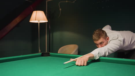 close-up shot of player in light shirt and dark trousers leaning over green pool table, gripping cue stick with deep concentration. eyes locked on cue ball, preparing for precise shot