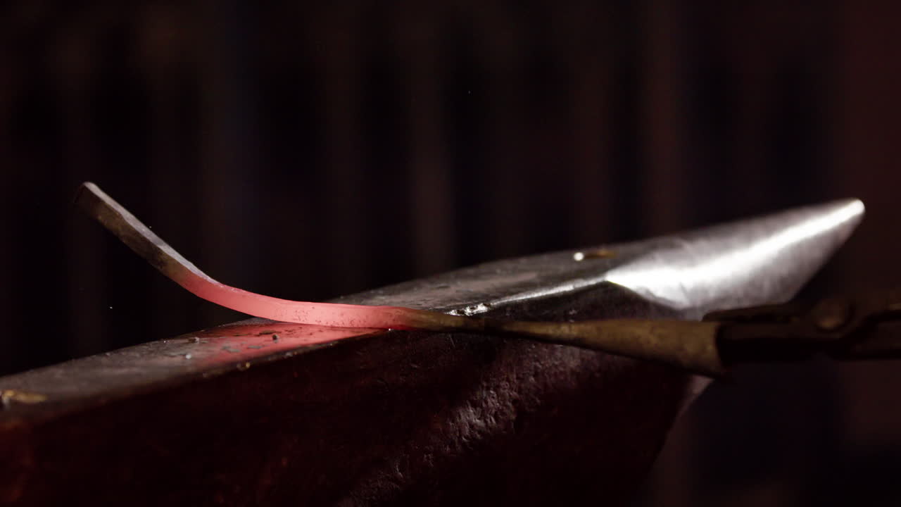 Closeup of a red hot glowing iron being hammered on an anvil, slow motion