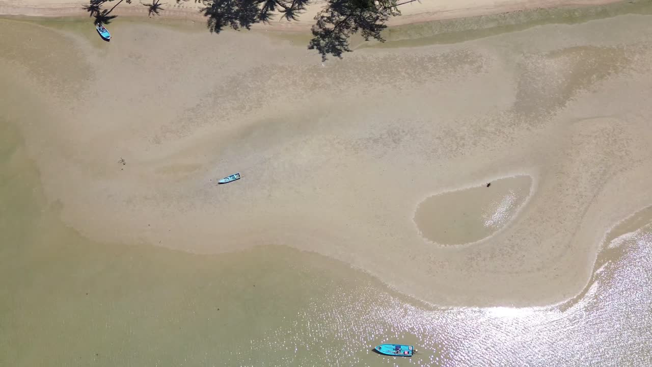 Captivating top-down drone footage showcasing traditional Thai fishing boats from directly above. The clear, shallow turquoise waters of Koh Phangan, Thailand