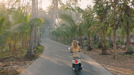 travel woman riding motorcycle on tropical island enjoying road trip adventure on motorbike scooter rear view