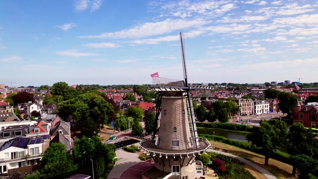 Hollanda'nın peynir pazarı şehri Alkmaar'daki Molen van Piet, güneşli mavi gökyüzü olan bir günde yukarıdan, arka planda şehir manzarası eski şehir ve dalgalanan şehir bayrağı ile görülüyor.