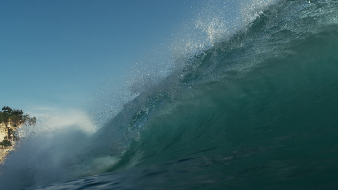 Curved wave face gliding forward with smooth motion over deep green sea, backlit glistening light