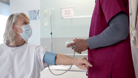 African-american-male-doctor-checking-blood-pressure-of-caucasian-female-patient-at-hospital