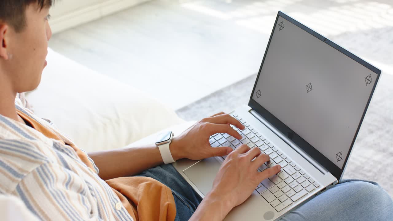 Uomo che digita al computer su un laptop color argento su un divano chiaro per lavoro