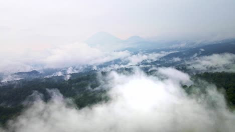 aerial-footage-above-a-vibrant-rainforest-with-an-active-volcano-in-the-backdrop,-highlighting-conservation-efforts,-aerial-4k-drone-footage