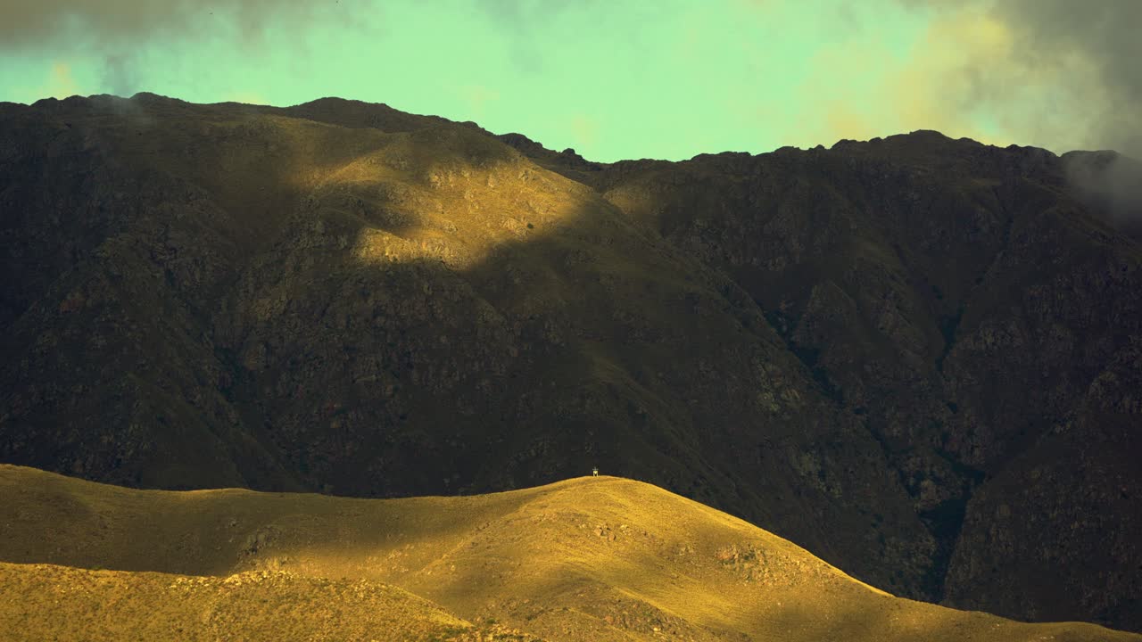 Pleasant view of clouds and shadows moving over the mountains during sunset. Bright yellow hill with a landmark at the top. Timelapse in 4k. Merlo, San Luis, Argentina.