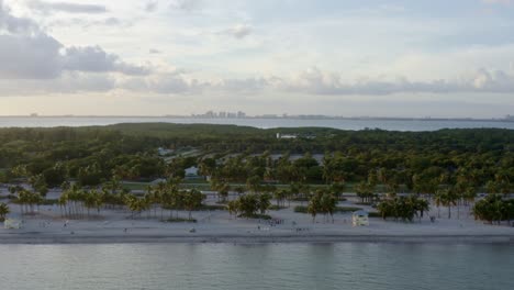 Toma-Aérea-De-Drones-En-Aumento-De-La-Hermosa-Playa-Tropical-Rodeada-De-Palmeras-En-El-Parque-Crandon-En-Key-Biscayne-En-Las-Afueras-De-Miami,-Florida,-En-Una-Cálida-Y-Soleada-Tarde-De-Verano.