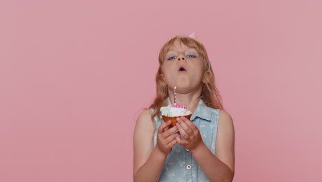 happy child girl kid celebrating birthday party, makes wish blowing burning candle on small cupcake