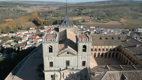 Vuelo-Ascendente-Y-Con-Un-Giro-De-Cámara-Vemos-El-Monasterio-De-Uclés-Con-La-Fachada-De-La-Iglesia-De-Nuestra-Señora-De-La-Asunción-Con-Sus-Torres,-El-Claustro-Y-El-Patio-De-Armas