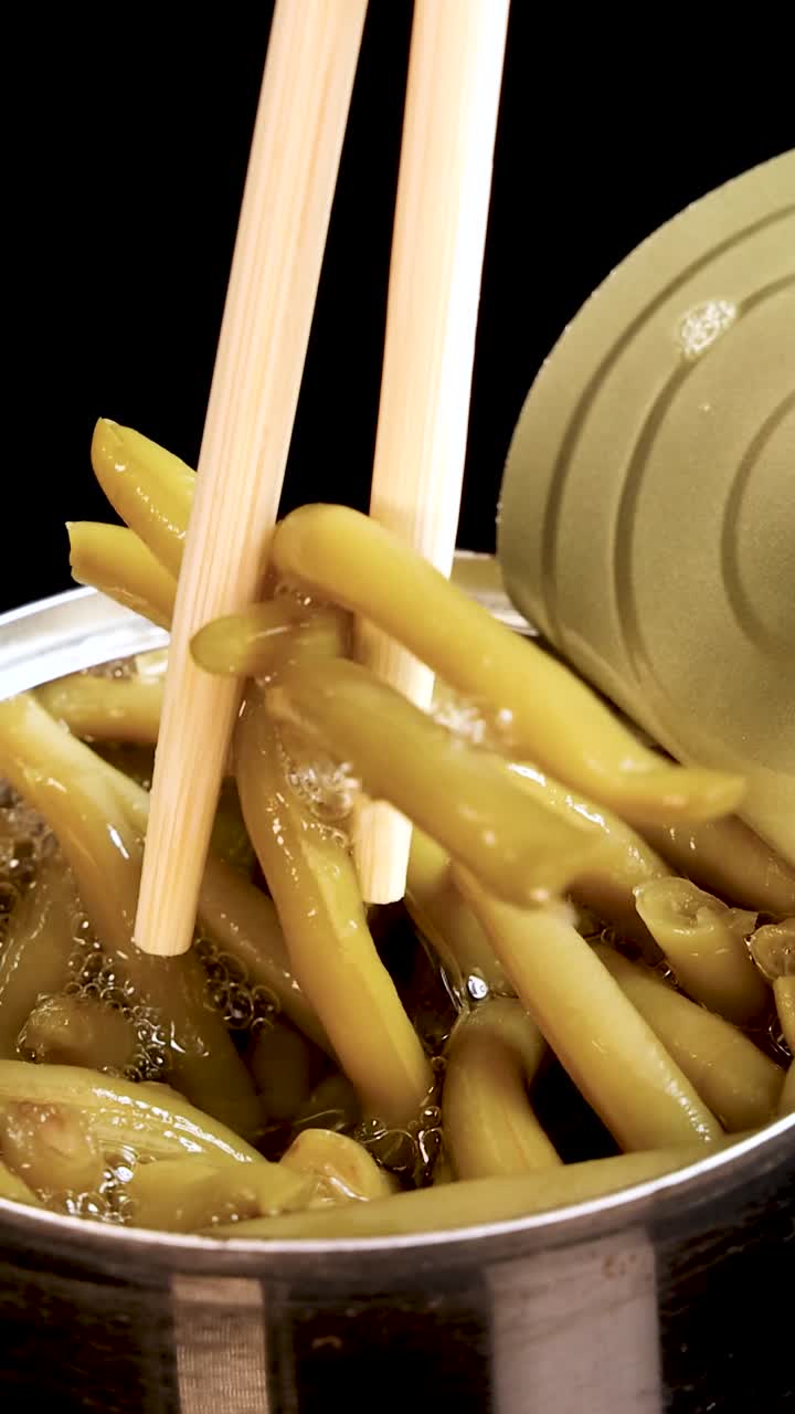 Close-up vertical shot of wooden chopsticks lifting haricot beans from a canned food container