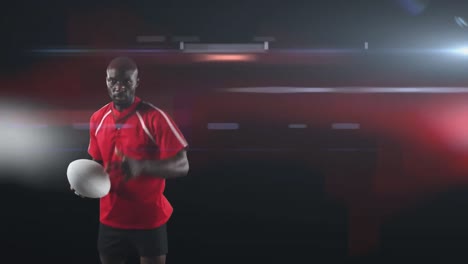 African-american-male-rugby-player-holding-rugby-ball-against-light-trails-on-black-background