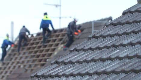 Medium-wide-shot-of-a-roof-with-tilers-working-on-another-roof-in-the-background