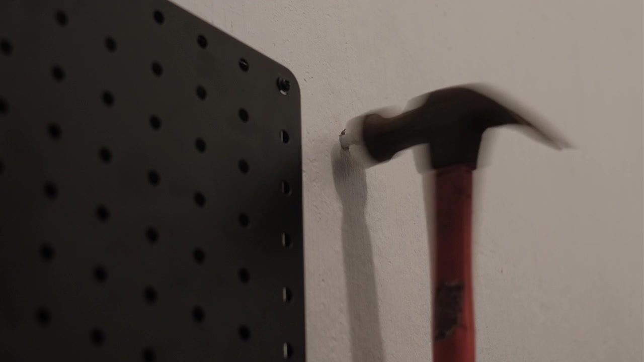 Primo piano di un martello che inserisce un tassello di plastica in un muro di cemento accanto a una parete forata nera durante lavori di installazione interni