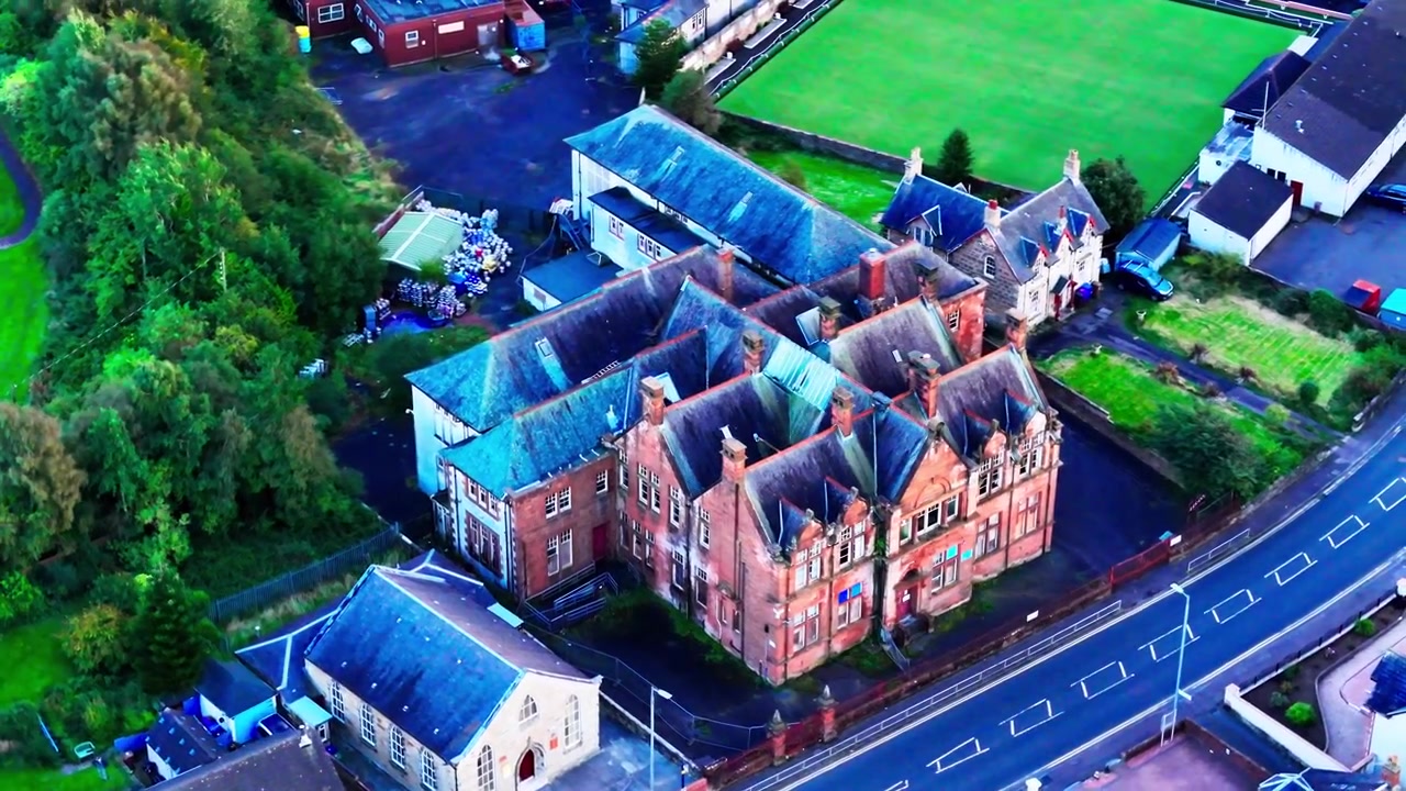 Kinematyczne ujęcie z drona śledzące historyczny, opuszczony budynek starej szkoły podstawowej w Dreghorn, Ayrshire, prezentujące porzuconą architekturę z czerwonej cegły.
