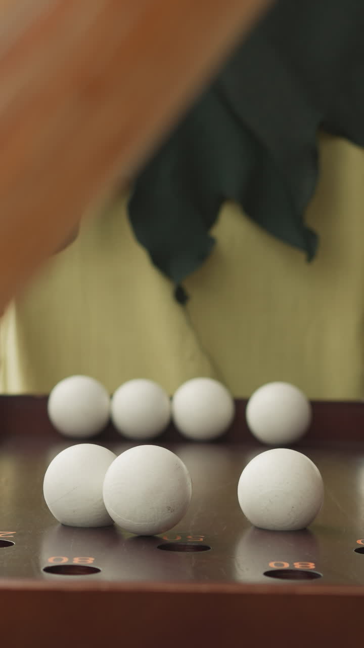 человек в костюме шутника стоит возле стола с деревянной настольной игрой с белыми шарами. человек готовится играть в неизвестный бадабум на размытом фоне