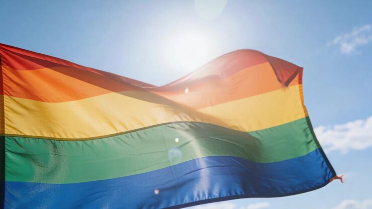 Bølgende regnbue pride-flag blafrer i sollys mod blå himmel, drevet af vinden, viser kanten
