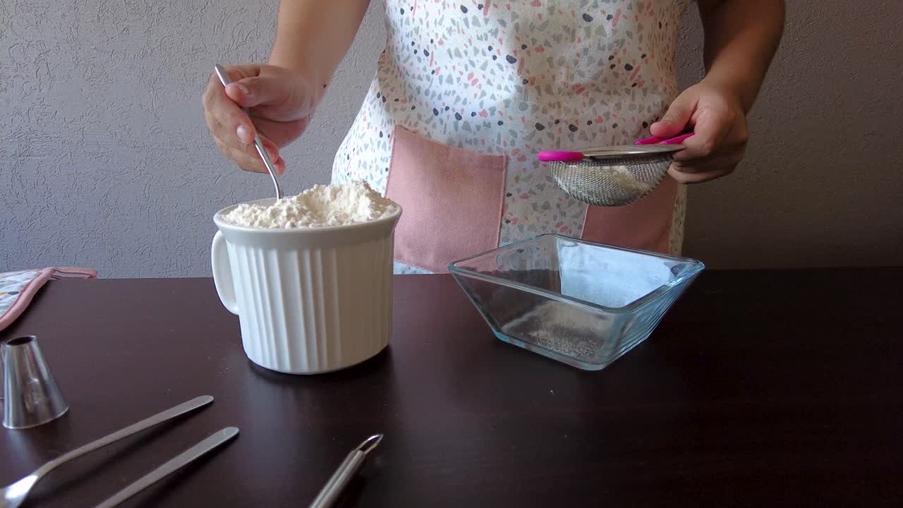 mujer latina con un delantal preparando la cocina horneando un pastel tamizando la harina usando un colador de metal y una cuchara para servir