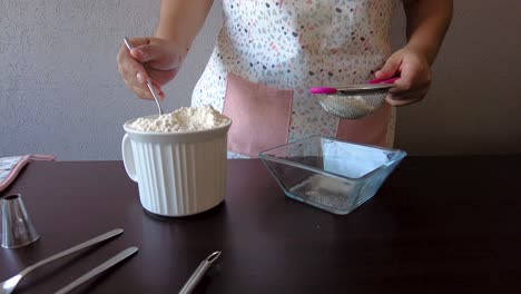 mujer latina con un delantal preparando la cocina horneando un pastel tamizando la harina usando un colador de metal y una cuchara para servir