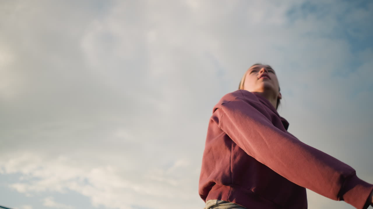 primer plano de una mujer con capucha sirviendo voleibol al aire libre, preparándose para servir con una fuerte acción de brazo en el campo abierto con cielo brillante y vegetación sutil en el fondo