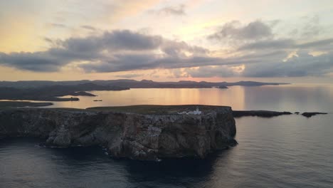 cavalleria lighthouse north of menorca sits with the sunsetting behind it on the edge of a cliff