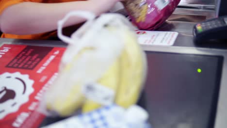 vista borrosa de un cajero en el supermercado con camisa naranja, el cajero escaneando las mercancías, comprobando con una tarjeta de crédito. primer plano de las mercancías