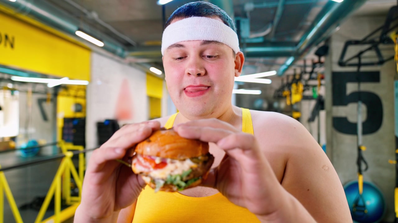 Uomo in sovrappeso tentato da un hamburger in palestra