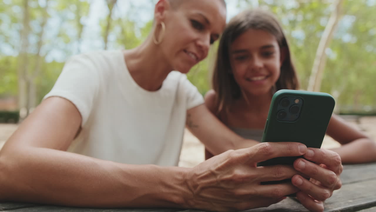 Happy Mother and Daughter Looking at Smartphone Together Outdoors