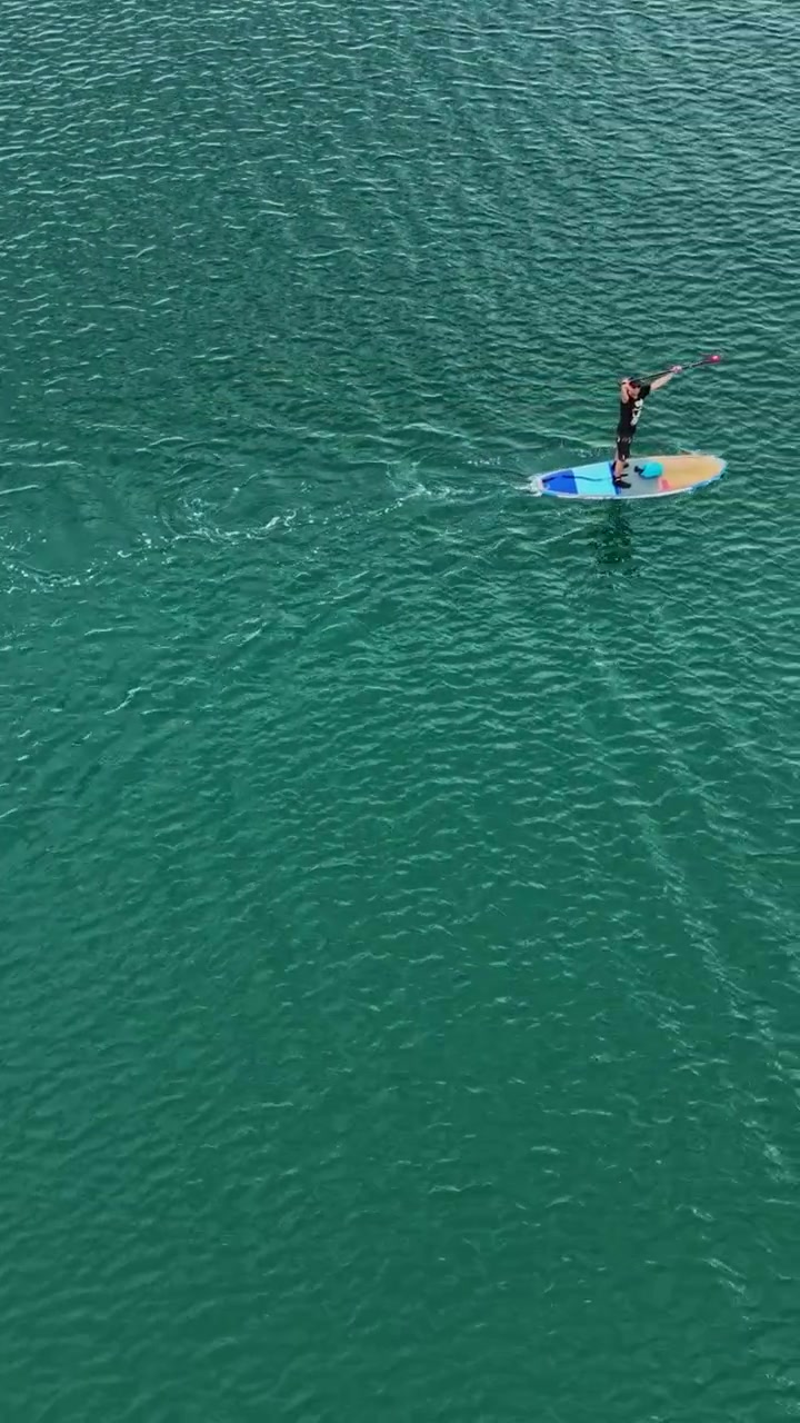 Persona che fa paddleboard su acqua limpida in una baia calma durante le ore diurne.