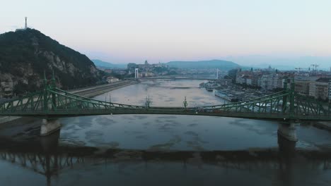 Vista-Aérea-Del-Tranvía-Que-Pasa-Por-El-Puente-De-La-Libertad-En-El-Río-Danubio-En-Budapest-Al-Amanecer,-Mañana